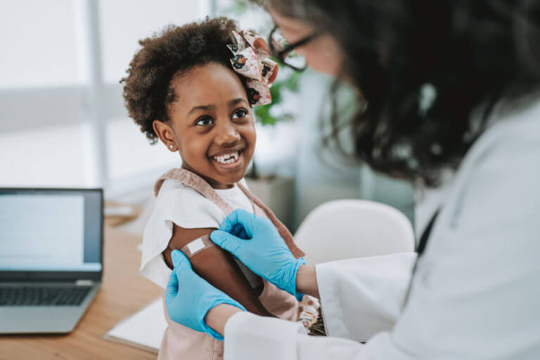 Child receiving vaccine from female doctor to keep up with immunization schedule.